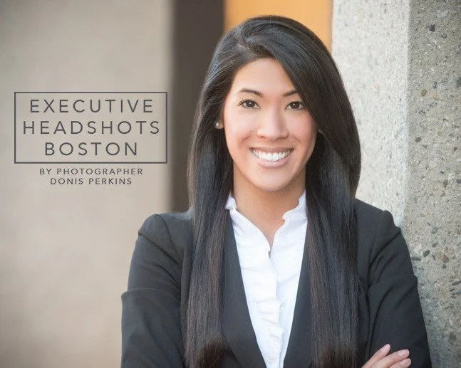 Smiling woman with long straight black hair in a black blazer and white shirt beside a concrete pillar